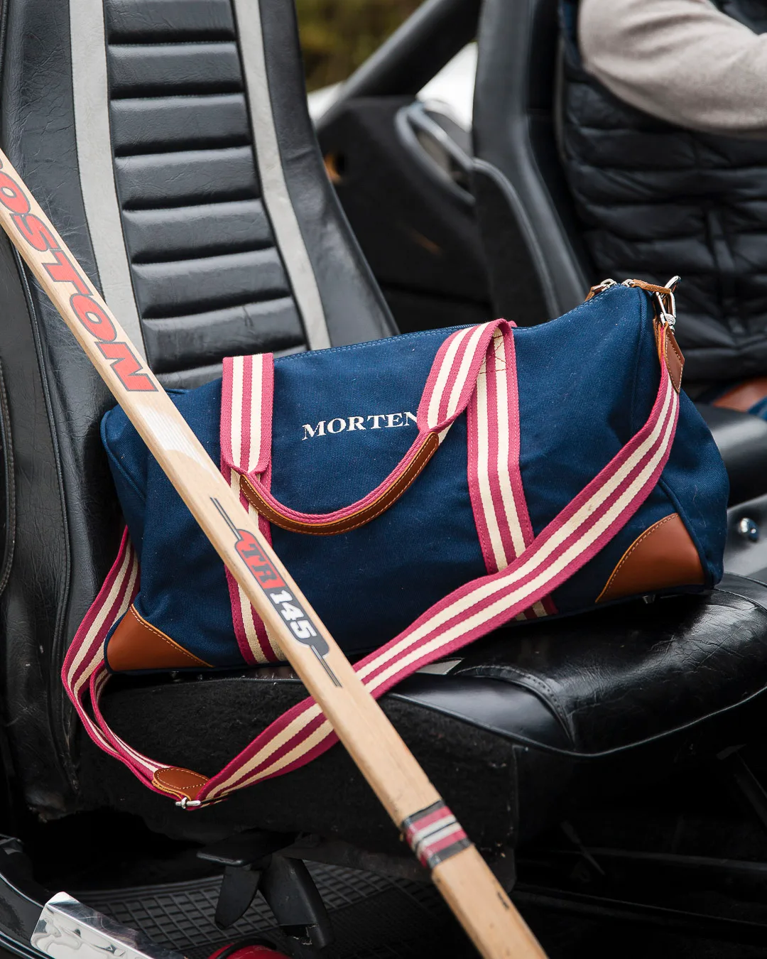 Retroinspirert bag i mørk blå canvas med stripete stropper i rødt og hvitt, og initialer brodert på fronten.