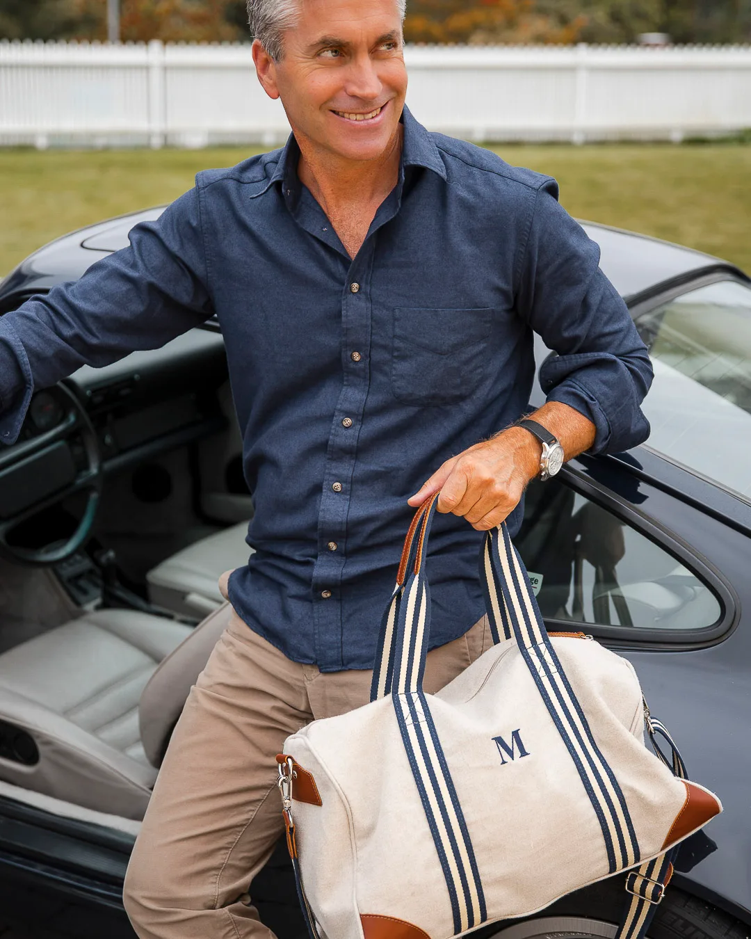Mann på vei ut av vintage Porche. Han har på seg mørkeblå skjorte og holder en bag i hånden.