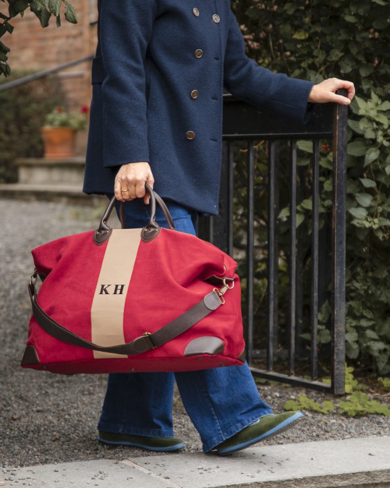 Kine bærer Harvard Stripe reiseveske i rødt og beige. Initialene KH er brodert på bagen i grått.