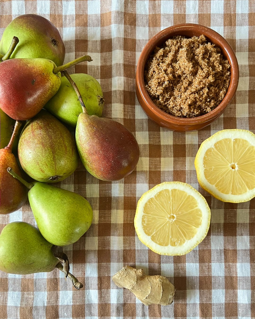 Pærer, brun sukker og sitroner på rustrød og hvit duk sett overnifra.