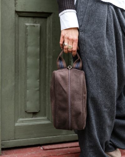 Kvinnehånd holder mørkebrun toalettmappe med brunt håndtak med mørkeblå detaljer.