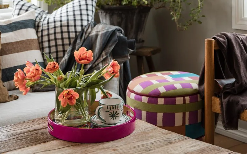 Utsnitt fra en stue. På stuebordet står en vase med tulipaner og en tekopp å et knallrosa brett. Ved siden av bordet skimter du en fargerik puff og en stol i skinn.