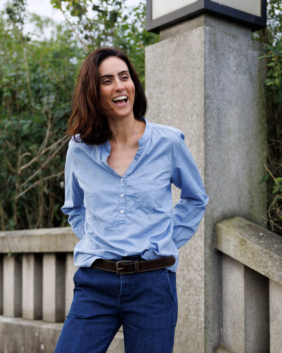 Kinne med mørkt hår ler. Hun har på seg en lyseblå bomullskjorte.