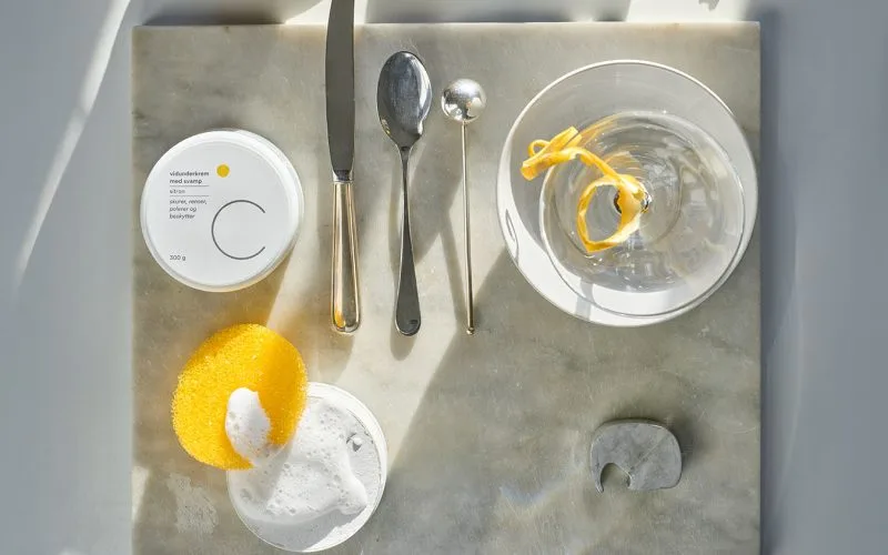 Csoaps vidunderkrem med gul svamp på marmorplate. Blankt bestikk og sollys som skaper vakre skygger.